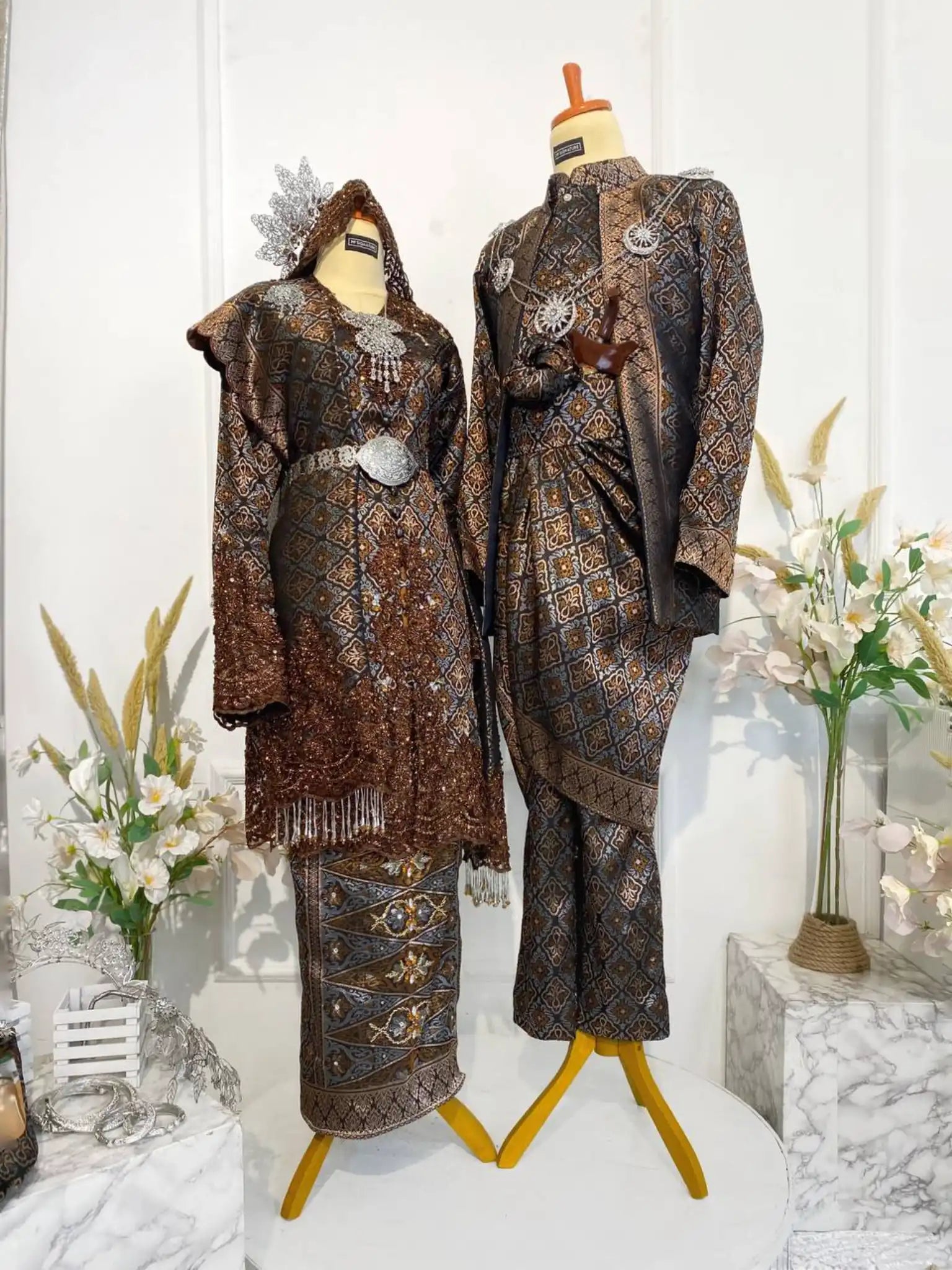 DARAWATI Baju Sanding Tradisional Dark Brown Songket Kebaya with Selempang Sulam Biku from Butik Pengantin PP Signature. This traditional wedding reception dress is crafted from luxurious Songket 3D fabric, featuring detailed silver and chrome accents.